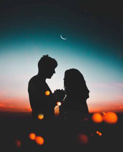 A silhouette of a young man and woman against the moonlight