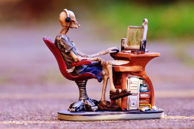 Sculpture of a skeleton sitting at a desk, using a computer