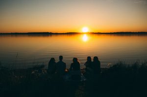 Five people sitting by water, watching sunset