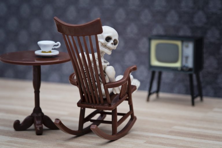 Skeleton in a rocking chair, trying to watch TV, and looking over his (its?) shoulder to the camera