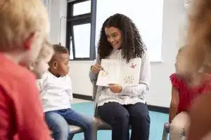 Black millennial woman teacher reading a storybook to her students.