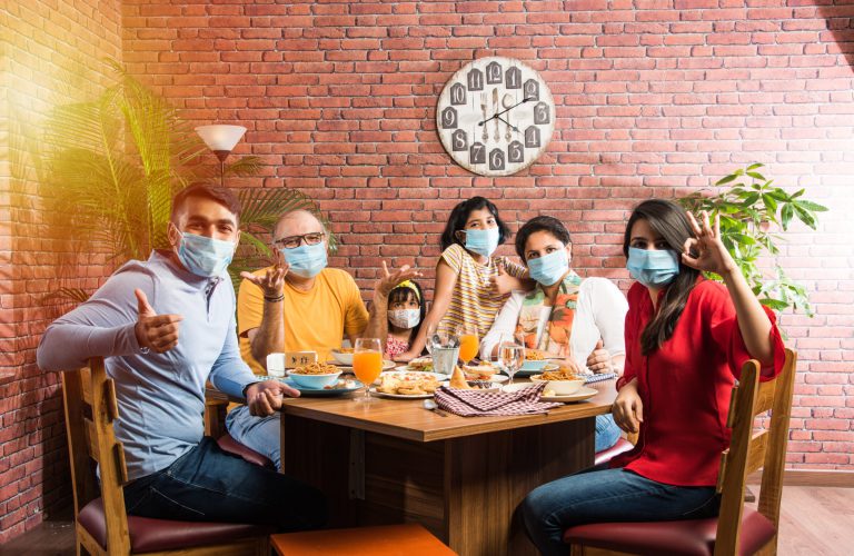 Family wears face masks while eating food in restaurant