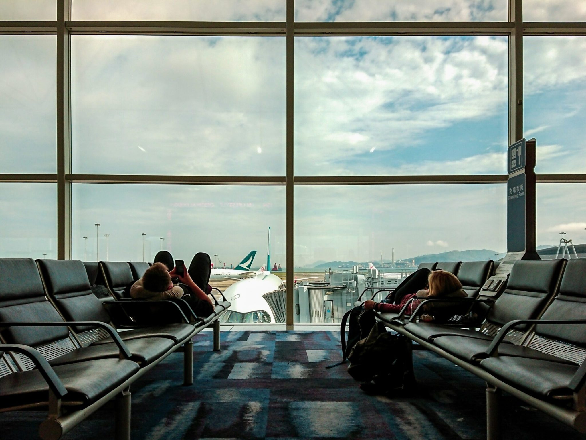 Two people lying down on benches in an airport lounge