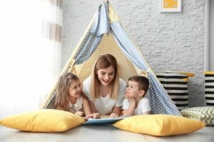 Nanny and little children reading book in tent at home