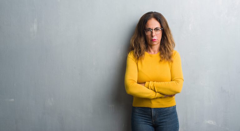 Middle age hispanic woman over grey wall wearing glasses skeptic and nervous, disapproving expression on face with crossed arms. Negative person.