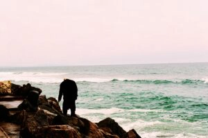 An elderly man stands on the rocks near the ocean