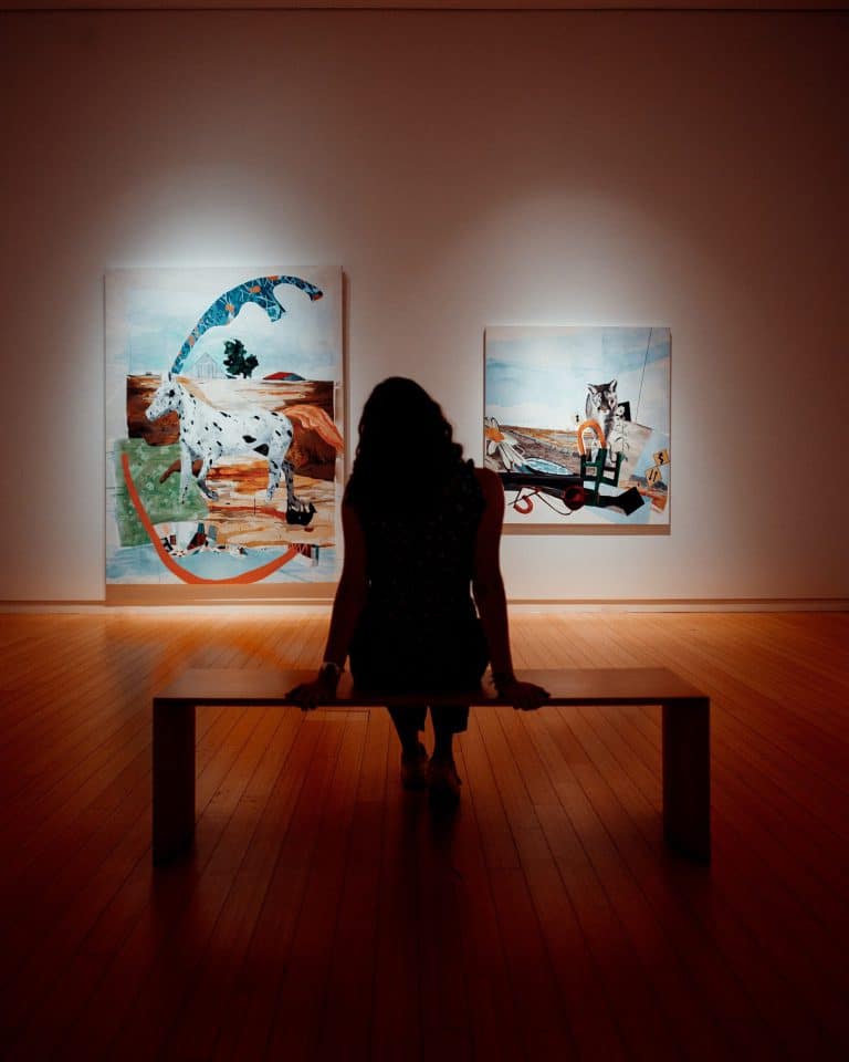 Woman sits in art gallery, looking at paintings