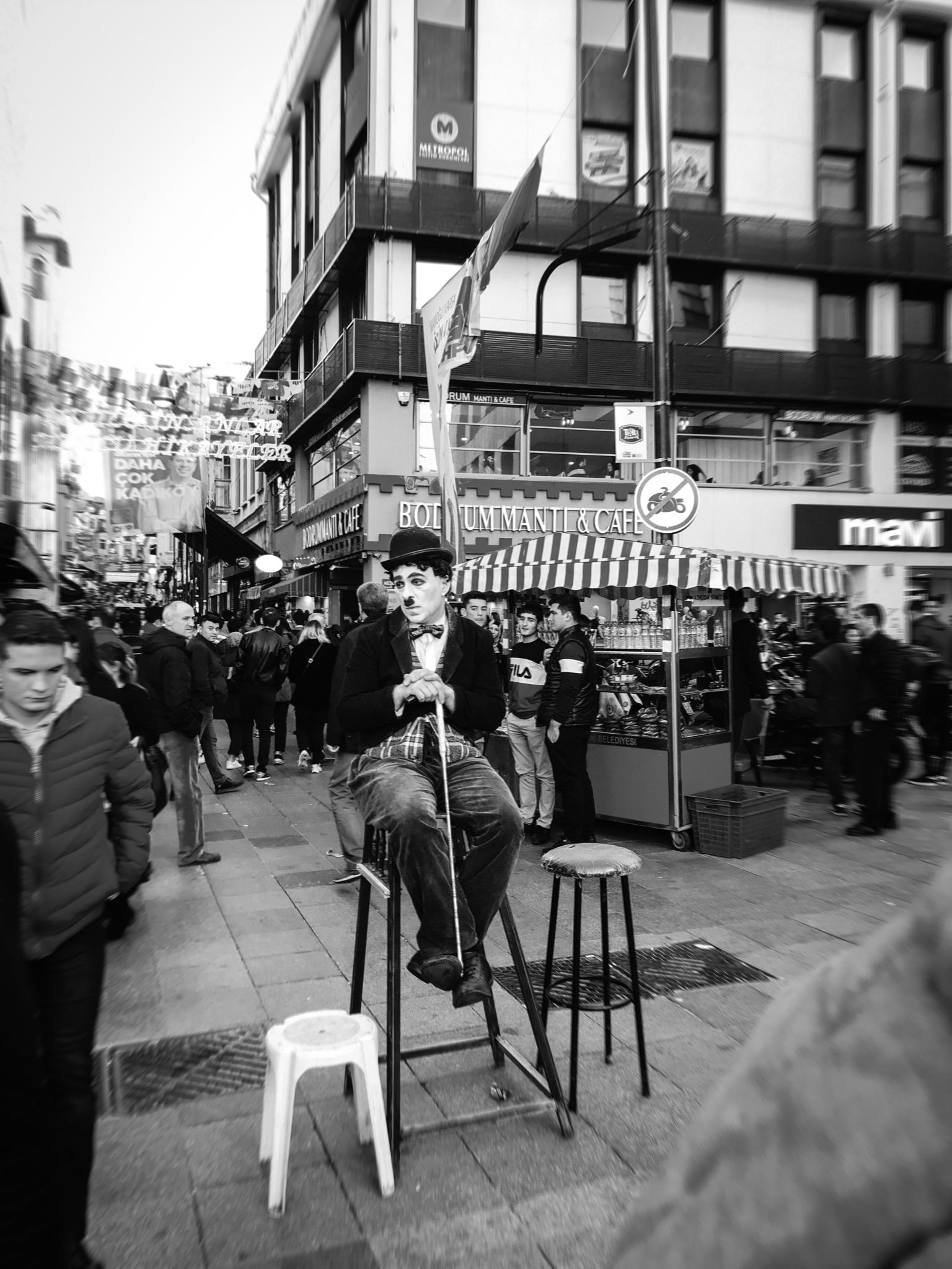 Charlie Chaplin impersonator sitting on a stool in a public market